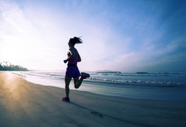 Genç, sağlıklı bir kadın plajda gün doğumunda koşuyor.