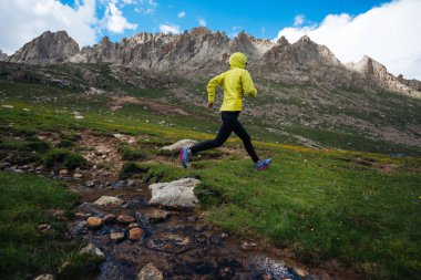 Kadın iz runner güzel dağlardaki küçük nehir üzerinde atlama