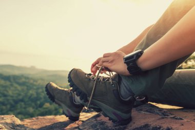 Başarılı yürüyüşçü oturup dağ zirvesinde ayakkabı bağı bağlama  