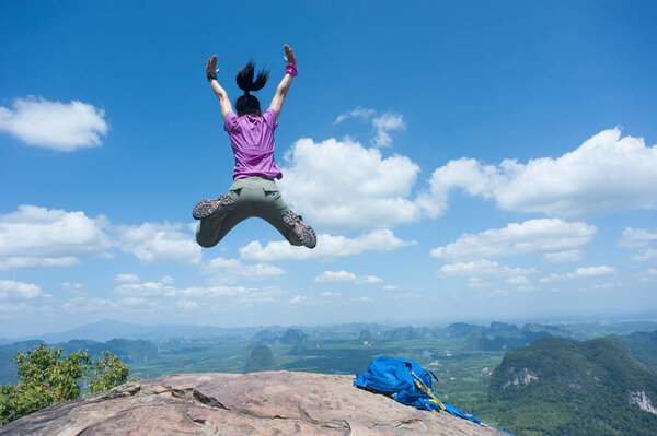 Счастливая успешная женщина-турист прыгает на вершину горы
  