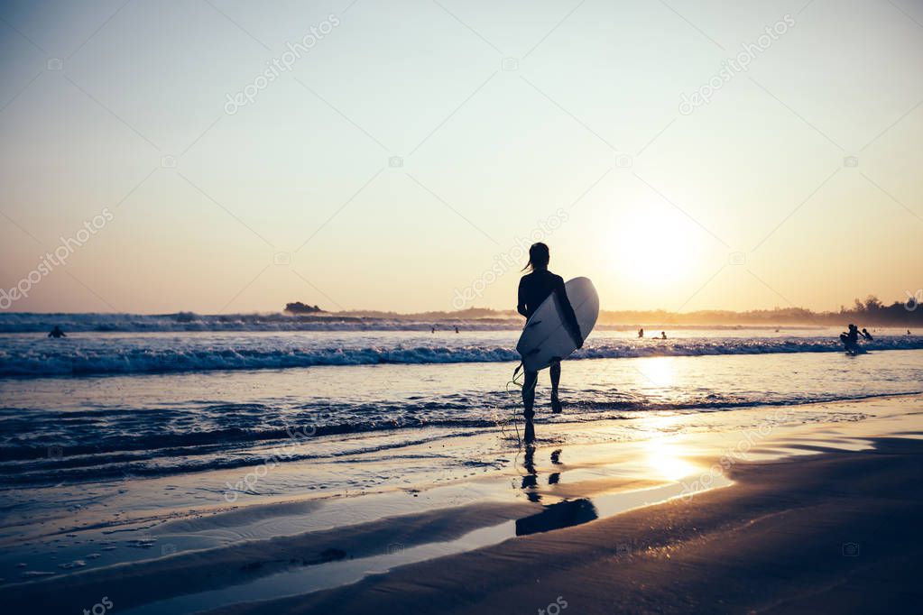Surfer woman walking with surfboard on sunset beach