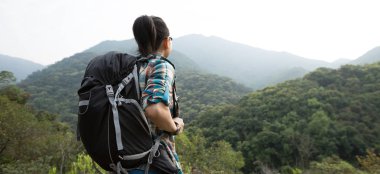 Sırt çantalı kadın dağ vadisinde bahar sabahı manzaranın tadını çıkarıyor.
