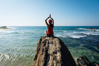 Genç yogacı kadın deniz kenarındaki kayalıklarda meditasyon yapıyor. 