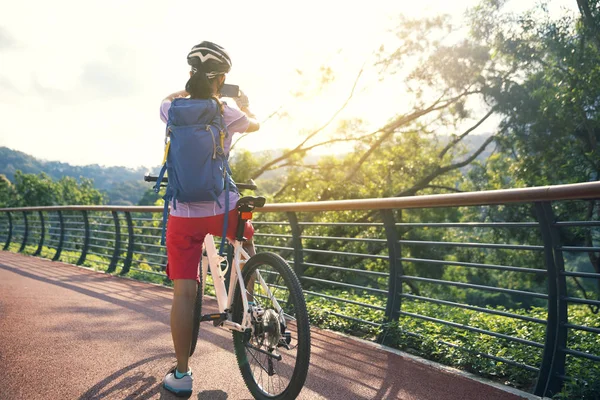 スマートフォンを使用してサイクリストと春の森のトレイルに自転車に乗っている間に写真を撮る — ストック写真