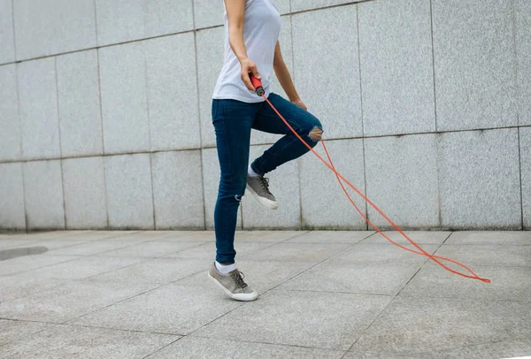 Young fitness woman with skipping rope against city wall