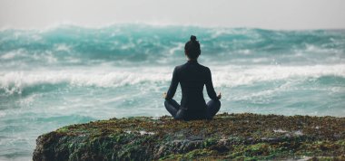 Mercan kayalığında dalgalarla yoga yapan bir kadın.