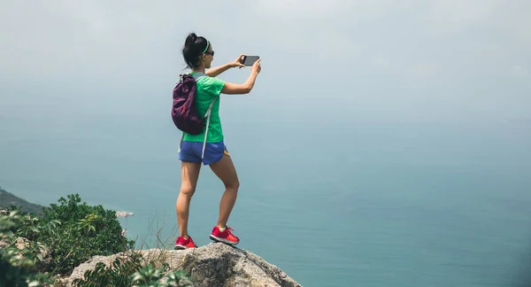 成功女子徒步旅行者拍照与智能手机在海边山顶 — 图库照片