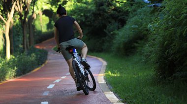 Güneşli park yolunda bisiklet süren bir kadın.