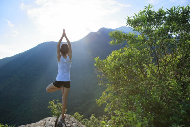 Dağ tepe uçurumun kenarında güneşin doğuşunu meditasyon yoga kadın
