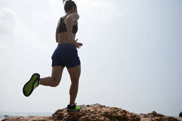 Woman ultramarathon trail runner running to rocky mountain top on seaside