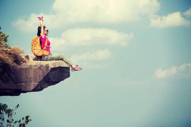 Başarılı kadın yürüyüşçü dağın tepesindeki kaya kenarında manzaranın tadını çıkarıyor