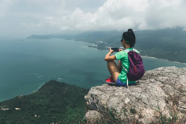 成功女子徒步旅行者拍照与智能手机在海边山顶 — 图库照片