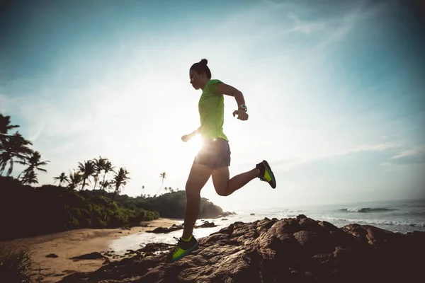 Young fitness woman trail runner running to rocky mountain top on seaside