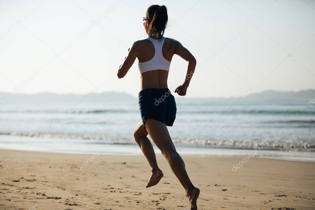 Young fitness woman running at sunrise beach 