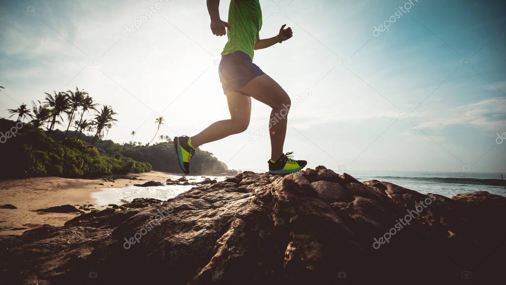 Young fitness woman trail runner running to rocky mountain top on seaside