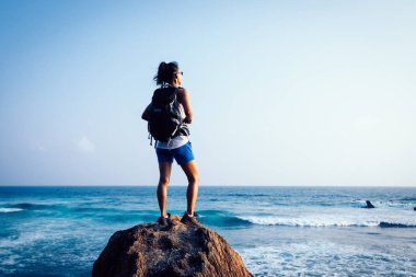 Genç kadın backpacker sahil rock uçurumun kenarında aşağı bakıyor