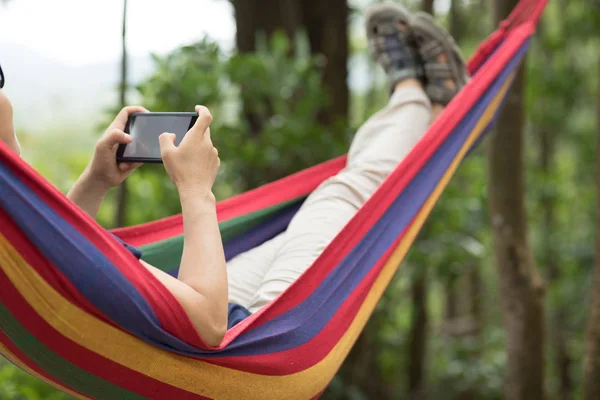 女人在吊床上放松与智能手机在森林 — 图库照片