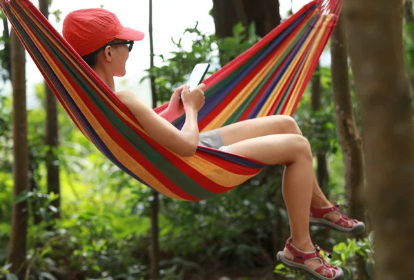 Woman Relaxing in hammock with smartphone in forest