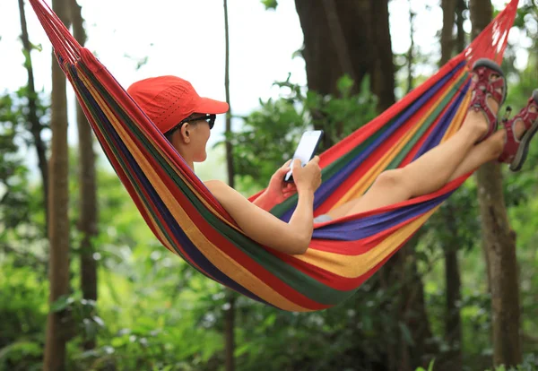 女子徒步旅行者放松在吊床上与智能手机在森林 — 图库照片