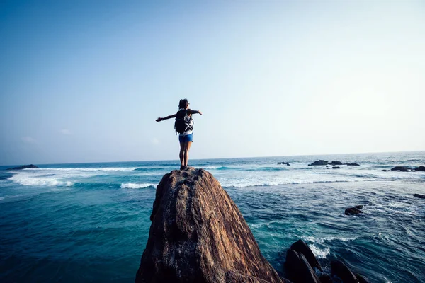 海辺の岩の崖の端に伸ばされた腕を持つ成功した若い女性ハイカー — ストック写真