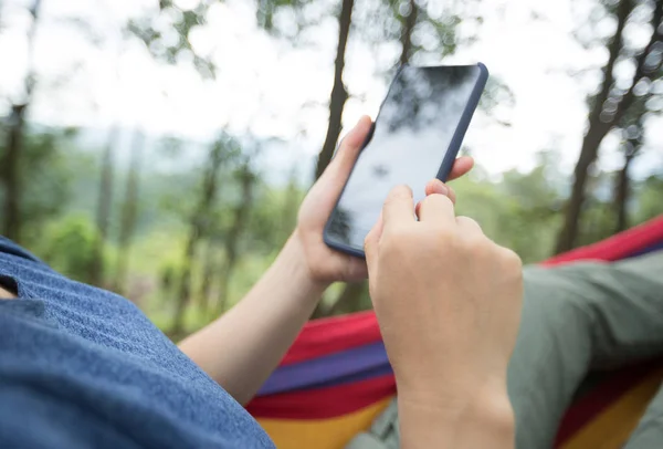 スマートフォンでハンモックでくつろぐ女性 — ストック写真