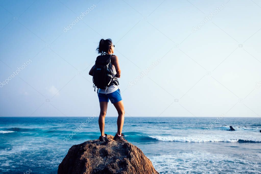 Young woman backpacker on seaside rock cliff edge looking down