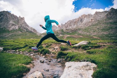 Kadın ultra maraton iz koşucu güzel dağlarda küçük nehir üzerinden atlama