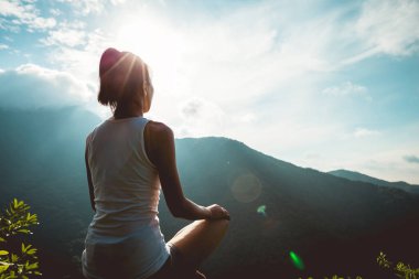 Dağ tepe uçurumun kenarında güneşin doğuşunu meditasyon yoga kadın