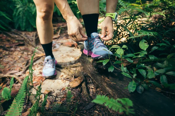 Woman ultra marathon runner tying shoelace on forest trail