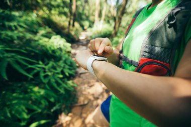 Asyalı kadın ultramaraton koşucusu tropikal orman parkurunda koşmadan önce spor saatini ayarladı