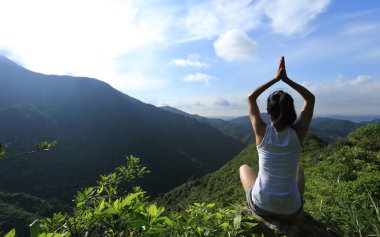 Dağ tepe uçurumun kenarında güneşin doğuşunu meditasyon yoga kadın