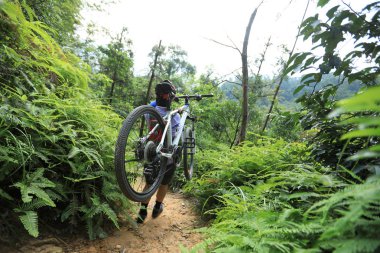 Tropik orman yolu üzerinde yürüyen dağ bisikleti taşıyan cross country bisiklet kadın bisikletçi