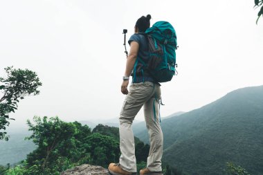 Dağın tepesinde ki uçurumun kenarında duran kadın yürüyüşçü aksiyon kamerasıyla selfie çekiyor