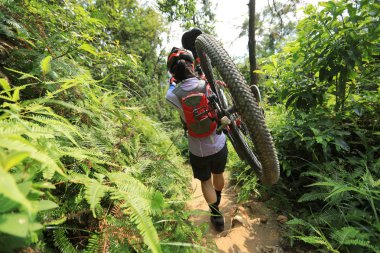 Tropik orman yolu üzerinde yürüyen dağ bisikleti taşıyan cross country bisiklet kadın bisikletçi