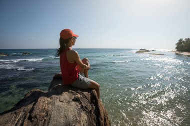 Sahil kenarındaki uçurumun kenarında oturan kadın yürüyüşçü manzaranın tadını çıkarın