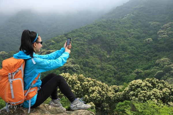 年轻女子的徒步旅行者使用智能手机自拍照在山的顶峰 — 图库照片