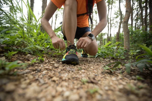 Woman ultra marathon runner tying shoelace on rainforest trail