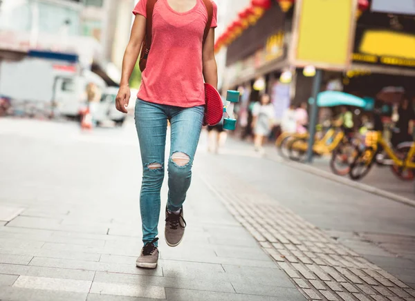 街でスケートボードを手に歩く女性 — ストック写真