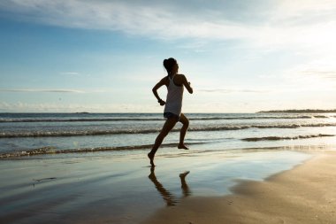 Fitness woman runner running on sunrise beach clipart