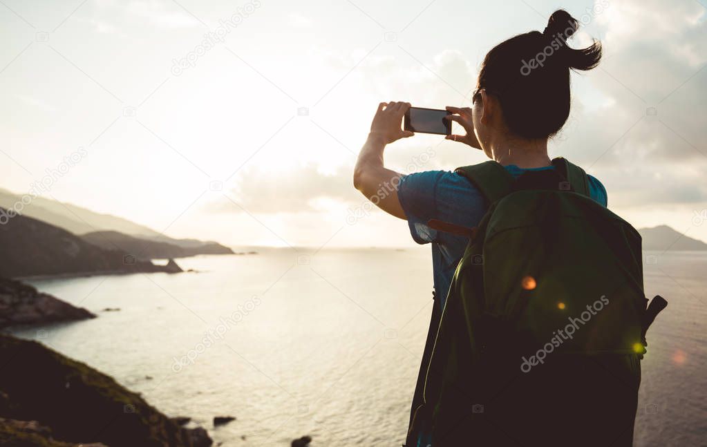 Woman hiking in seaside taking pictures with mobile phone