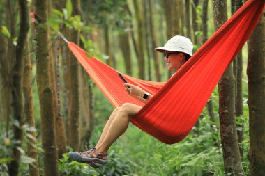 Hamakta dinlenen bir kadın yağmur ormanlarında akıllı telefonuyla