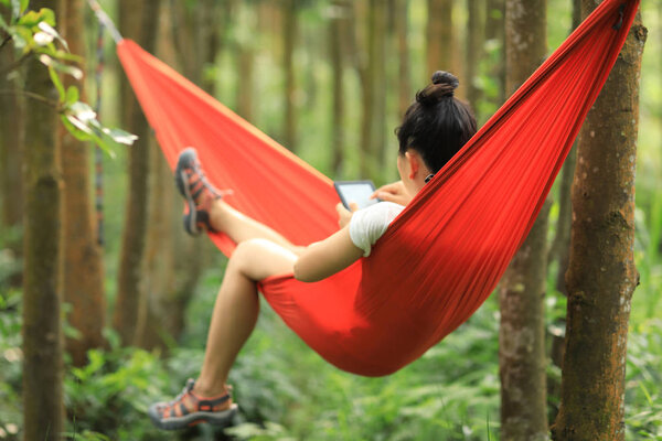 Relaxing in hammock reading ebook in tropical rainforest