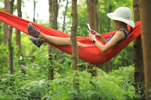 在热带雨林里用智能手机在吊床上放松的女人 — 图库照片