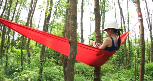 熱帯雨林でスマートフォンでハンモックでくつろぐ女性 — ストック動画