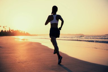 Güneş doğarken plajda koşan fitness kadın koşucusu