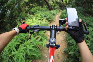 Yağmur ormanı parkurunda bisiklet sürerken akıllı telefon kullanan bisikletçi