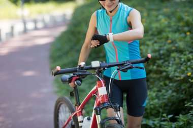 Bisikletli bir kadın güneşli bir günde bisiklet sürerken akıllı sepetine bakıyor.