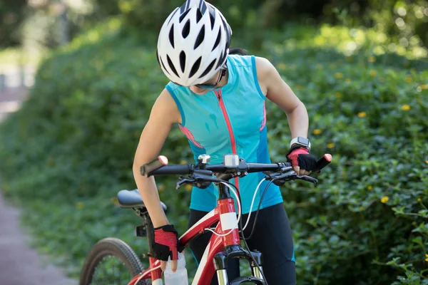 公園の自転車道に乗って 晴れた日に自転車に乗っている間 女性サイクリストは水を飲みます — ストック写真