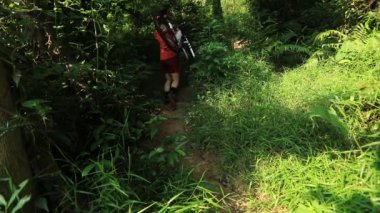 Tropik orman yolunda dağ bisikleti taşıyan kadın bisikletçi, yavaş çekim 