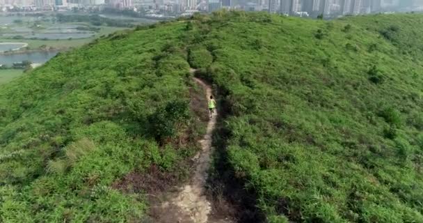 背景に都市と緑のトレイルで走る女性ウルトラマラソンランナーの航空写真 — ストック動画